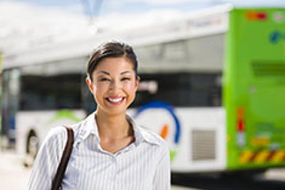 Head and chest shot of smiling lady in officewear, standing face-on smiling with bus behind her