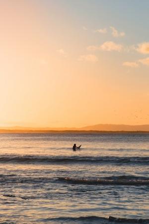 Image of the ocean looking into the sunset with one surfer paddling